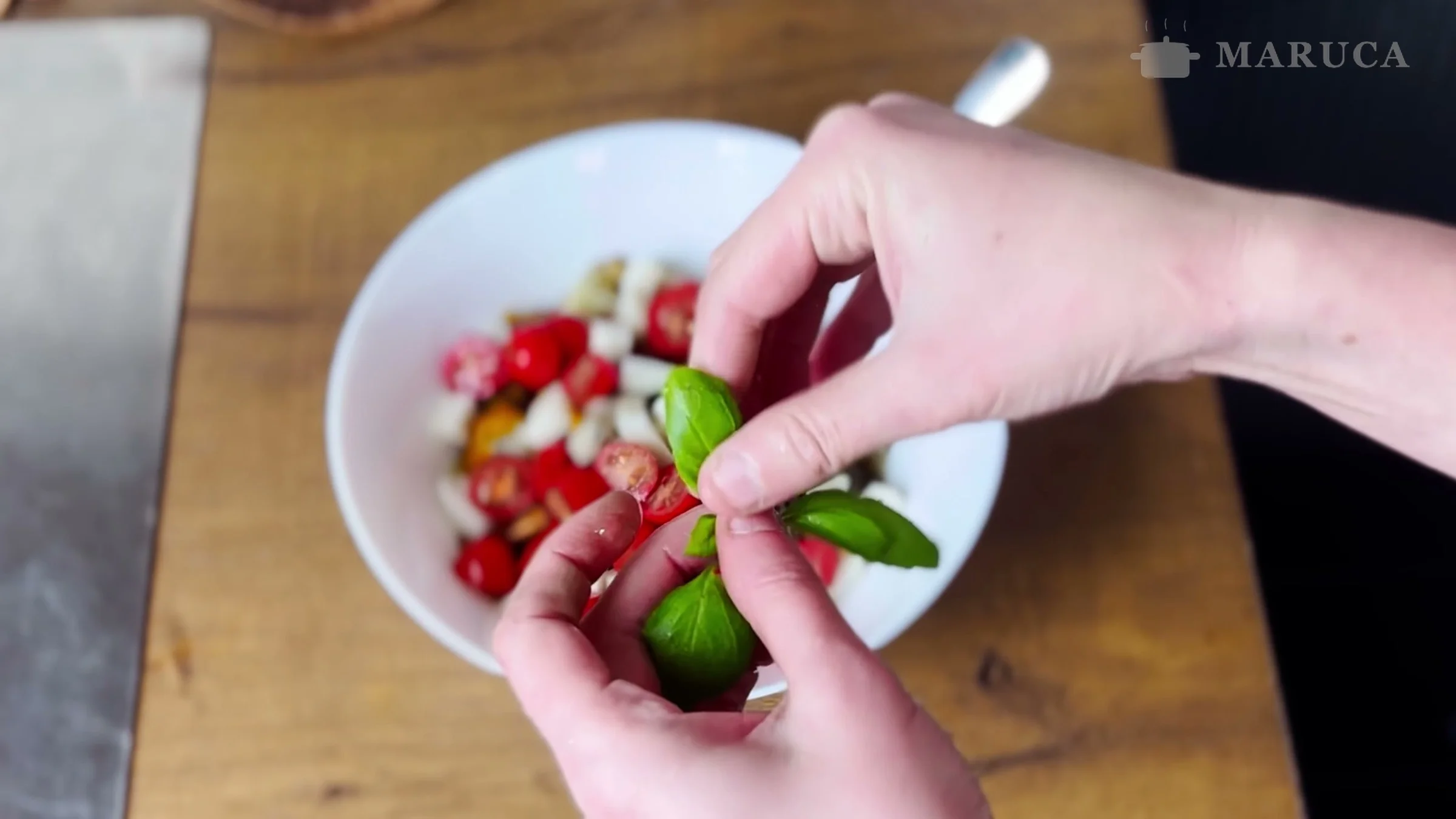Agregando hojas de albahaca a la ensalada con tomates y queso