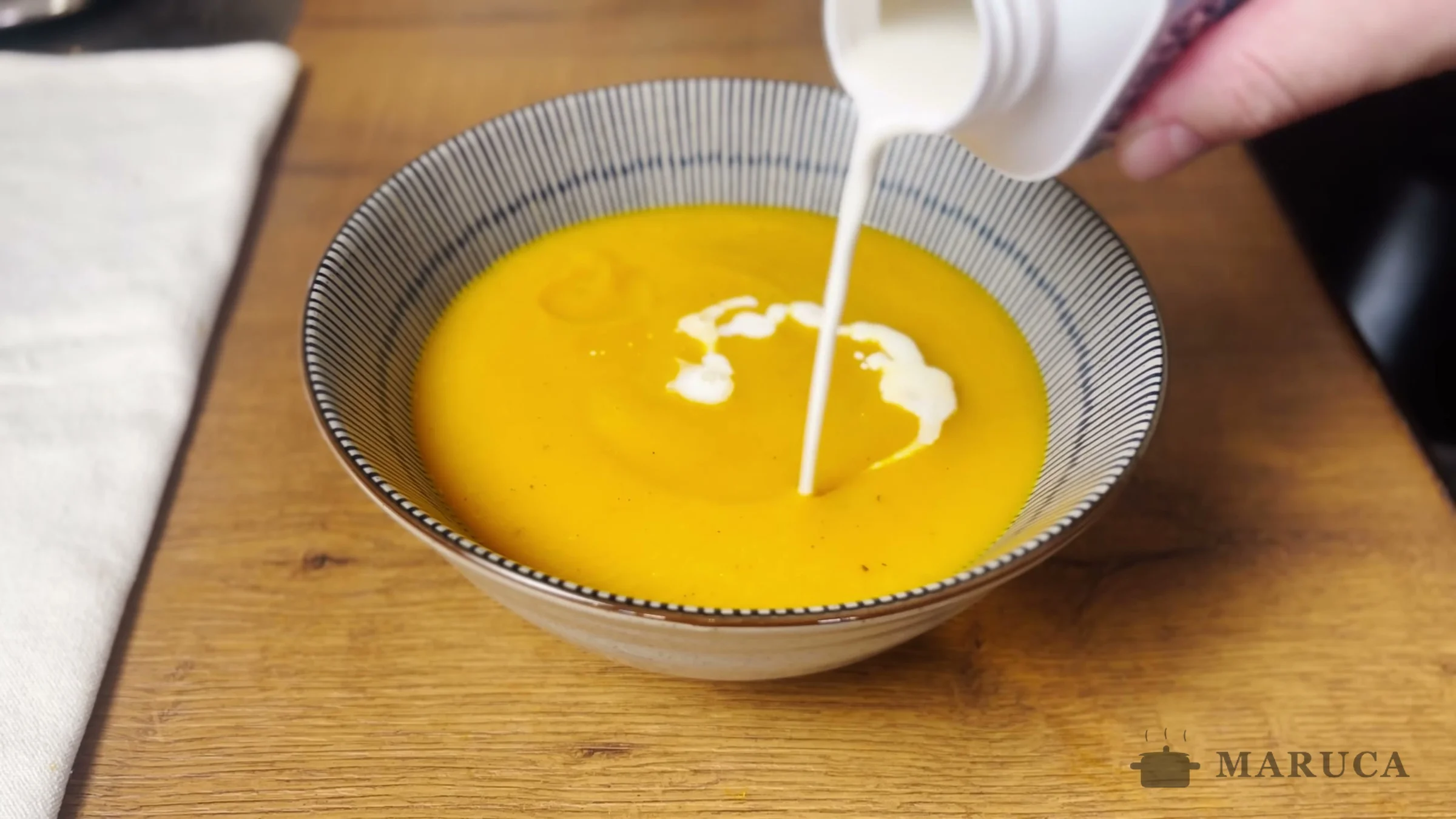 Chorrito de crema de leche cayendo sobre la sopa crema de zapallo en un bowl