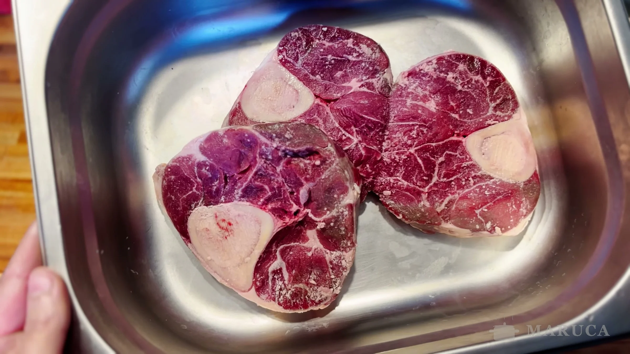 Tres rodajas de osobuco crudo con el hueso y el caracú en una bandeja de acero