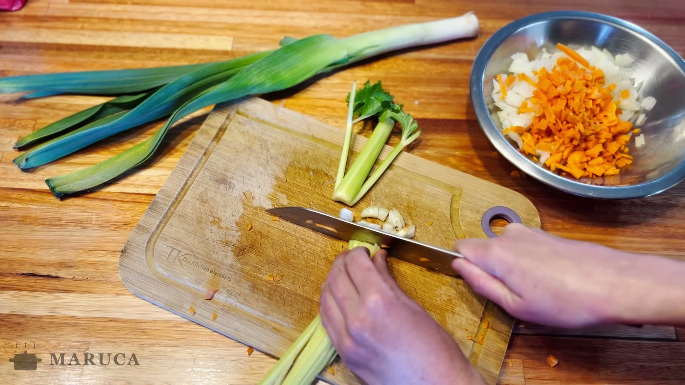 Picando apio y puerro sobre la tabla con la cebolla y la zanahoria ya picadas en un bowl
