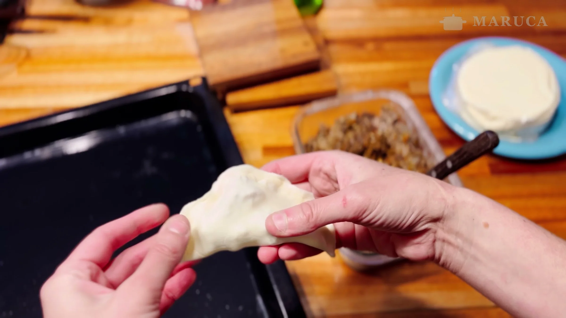 Cerrando una empanada de osobuco con las manos sobre la asadera