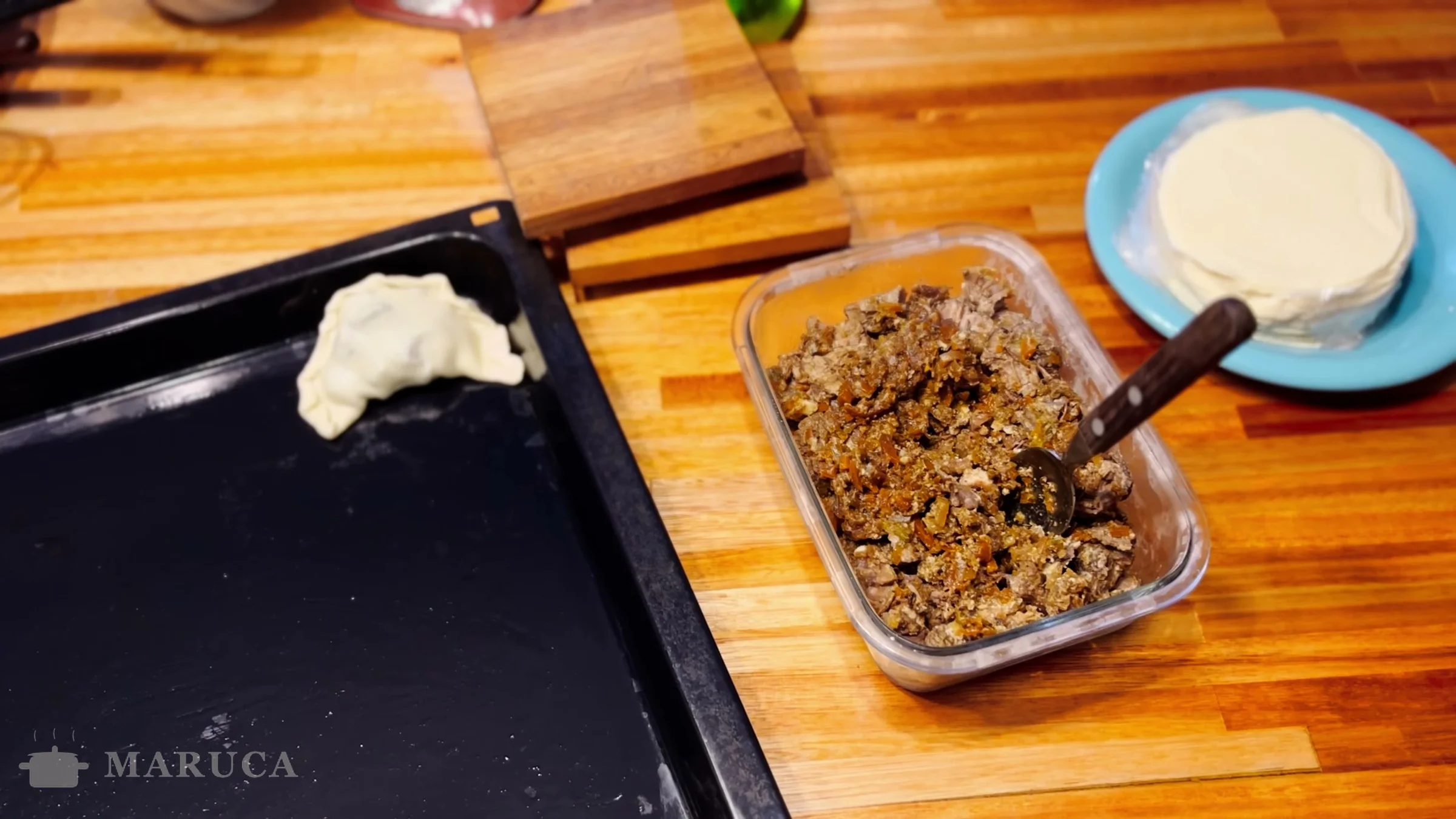 Primera empanada con repulgue en la asadera junto al táper de relleno y las tapas