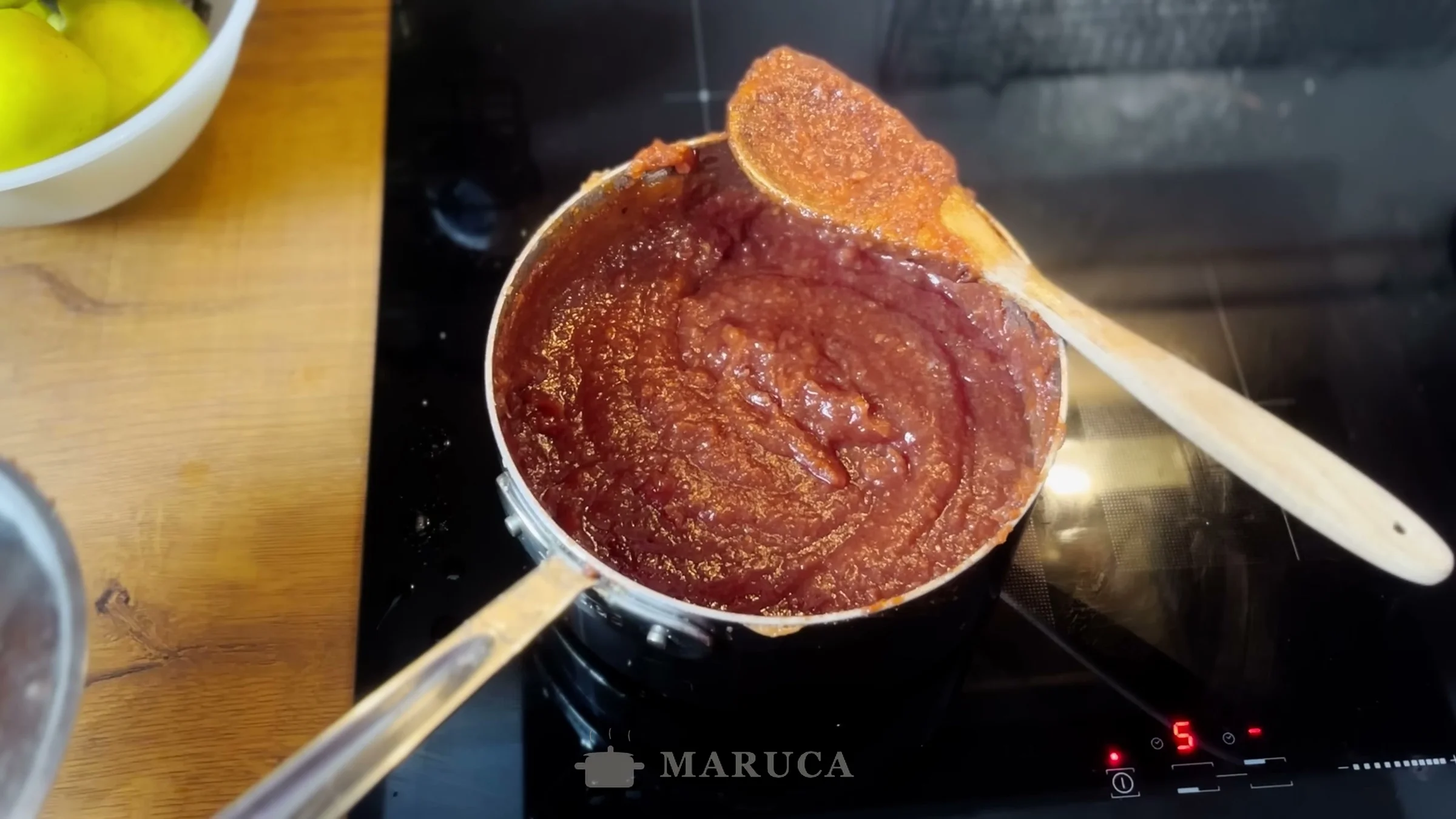 Dulce de membrillo rojizo cocinándose en la cacerola con cuchara de madera
